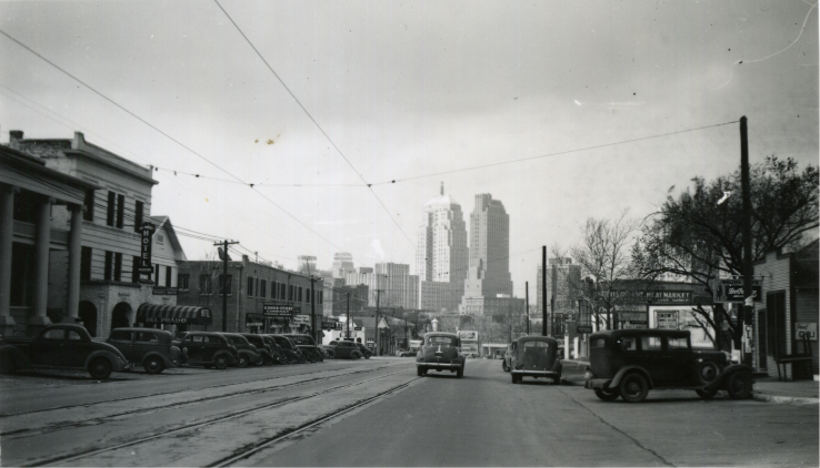 Looking down a downtown Oklahoma City street with streetcar overhead wires and the city skyline beyond, c. 1930s–40s